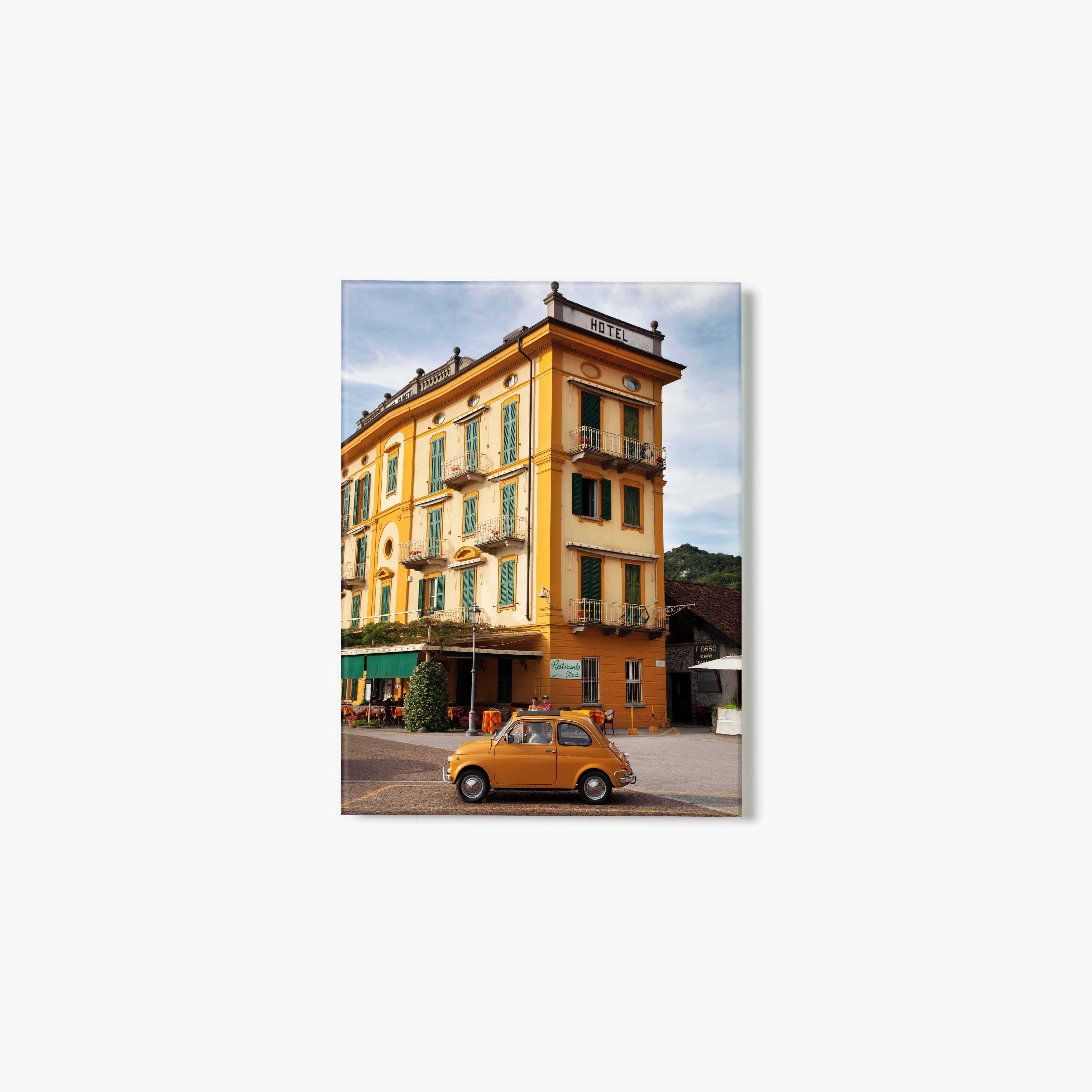 Yellow vintage car parked in front of a yellow hotel with green shutters.