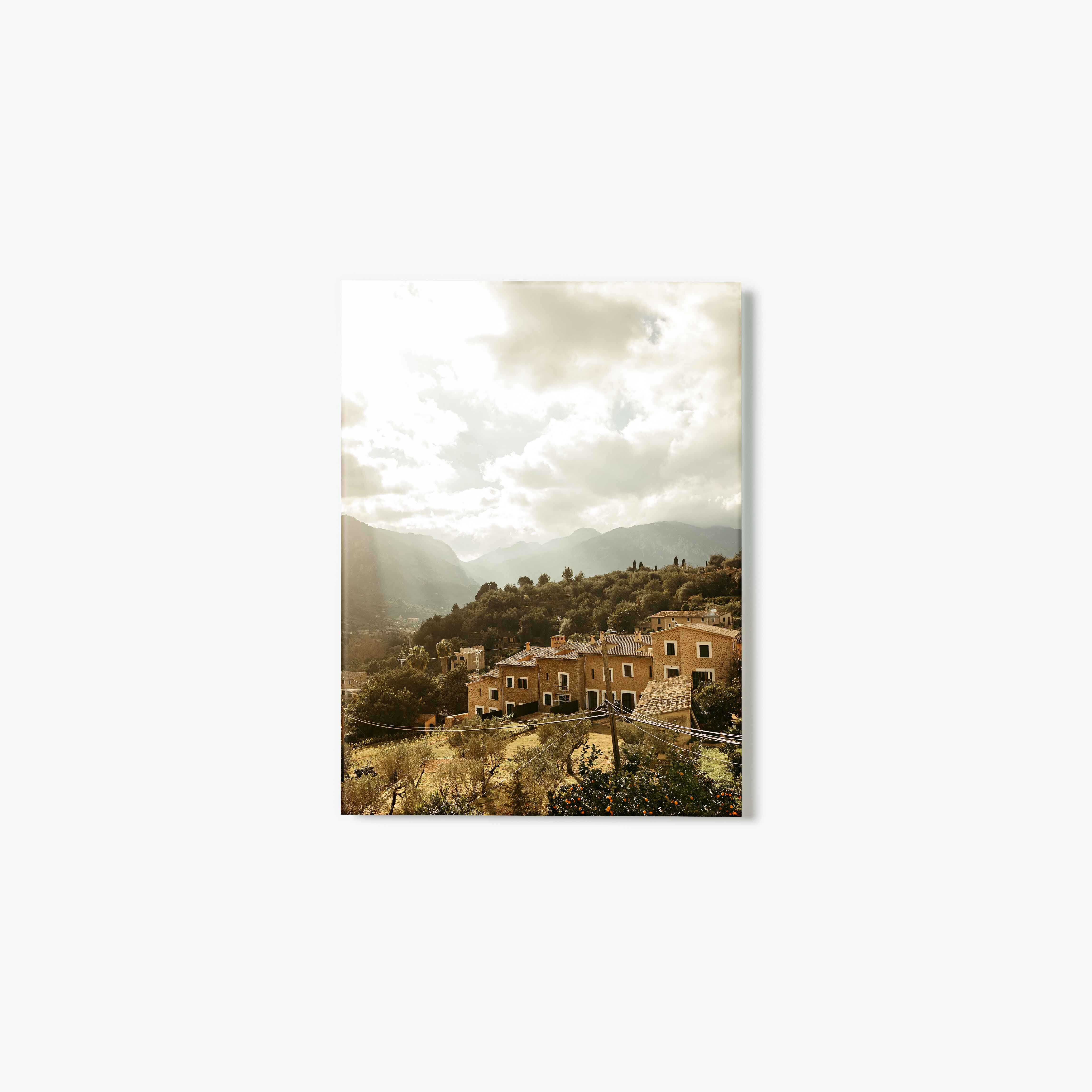 Glass print of a village with houses and mountains under a cloudy sky