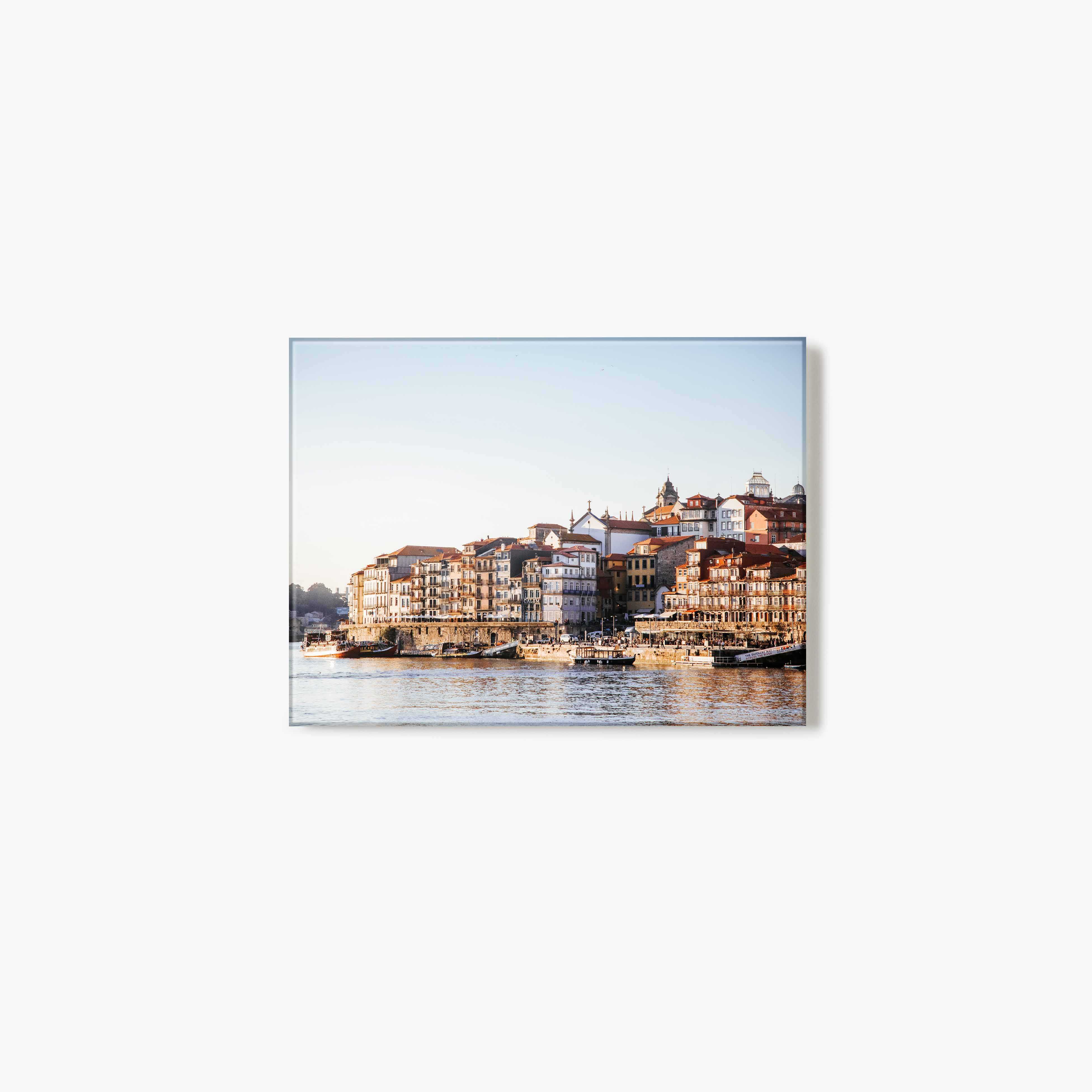 Glass print of a the Porto riverside with buildings along a waterfront and a golden glow from the sun.